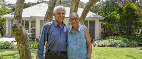 A couple smiling, standing in front of their house