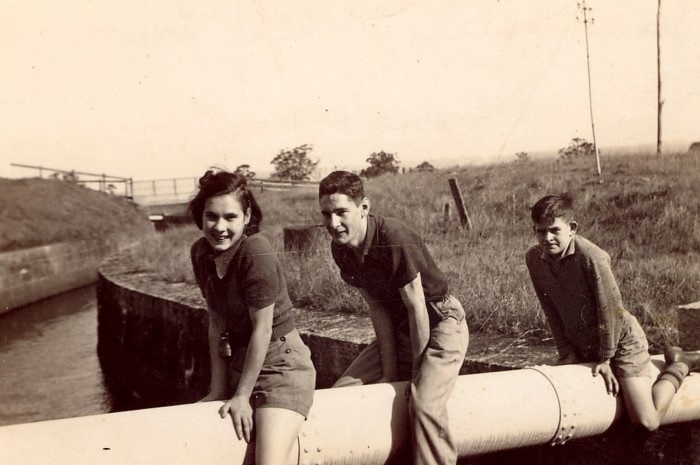 3 teenagers sitting on a large water pipe over a canal