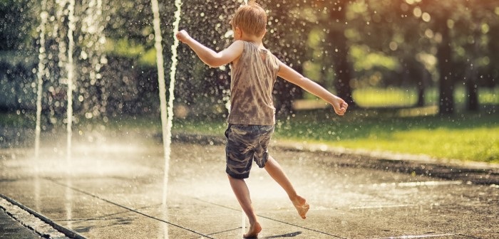 White child in singlet and shorts playing in a public water fountain