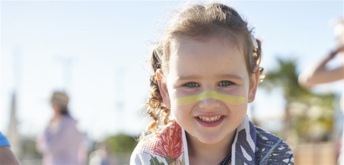 A smiling young girl with zinc on her face poses for the camera