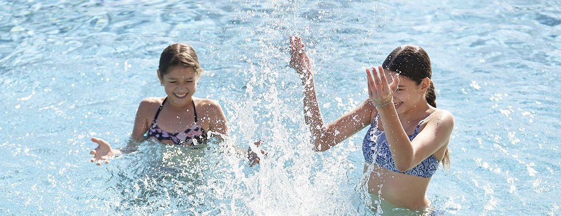 Two girls having fun in a pool, splashing water