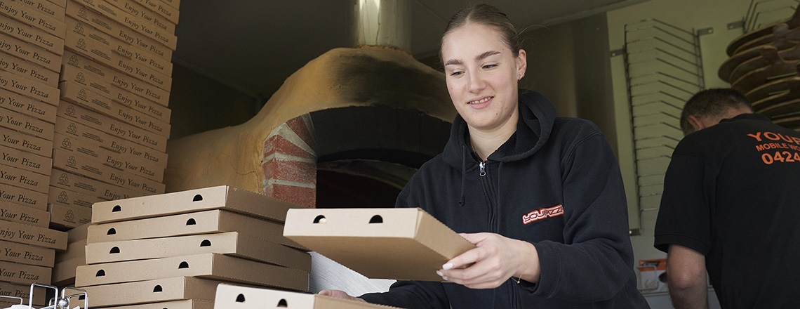 An employee of a pizza food truck hands out pizzas