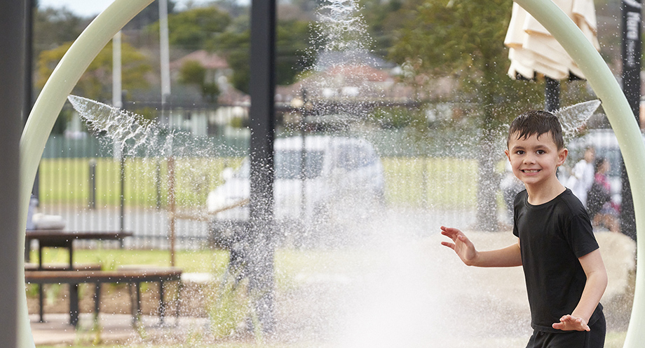 A young boy smiling at the camera while playing in the splash park at the Billabong