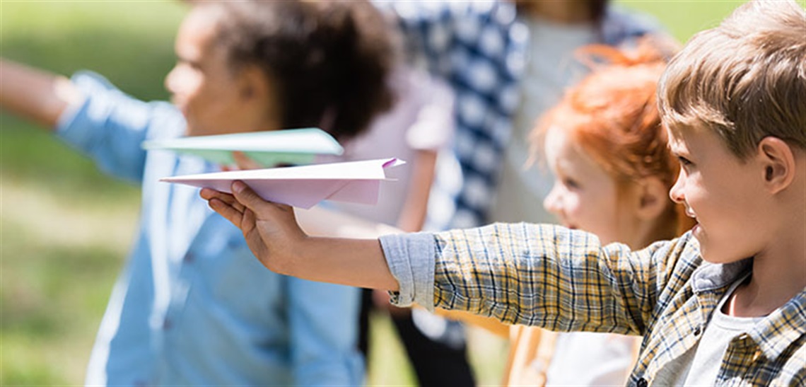 Kids holding paper planes in a park