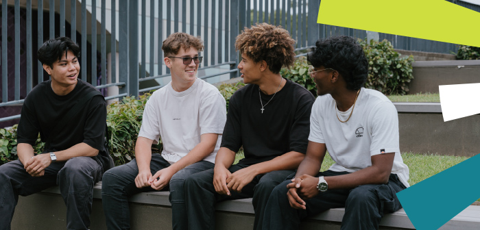 A group of four young males sitting down and talking outside