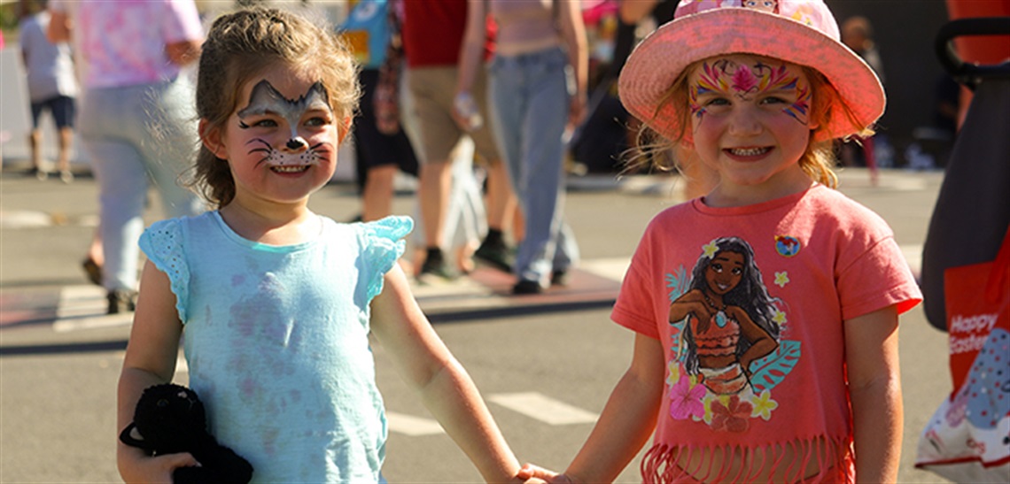 Two girls with their faces painted, holding hands ands smiling