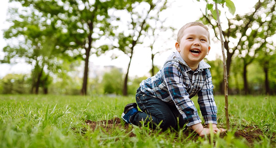 A photo of a young boy, smiling while kneeling next to a tree