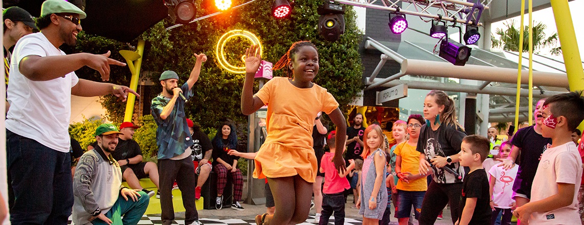 A young girl dances while a crowd of people look on