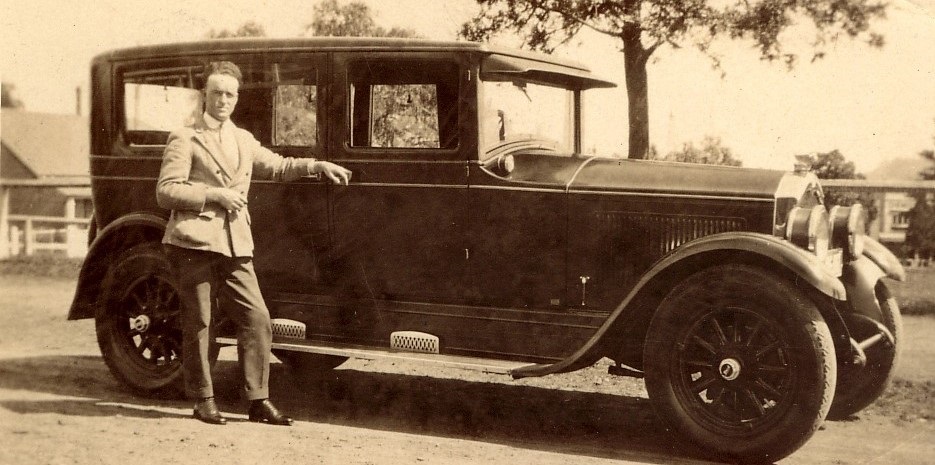 A well dressed gentleman leaning on his car